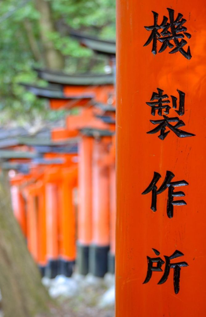 Close-up of vibrant orange torii gates with Japanese characters in Kyoto, Japan.